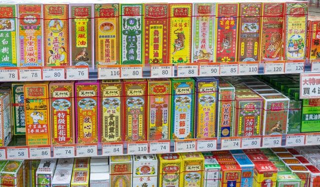 特写展示药店货架上整齐排列的金波士等多种传统中成药，包装色彩鲜艳，带中文标签与价格牌，光线充足，画面清晰稳定，呈现药房药品陈列场景。
